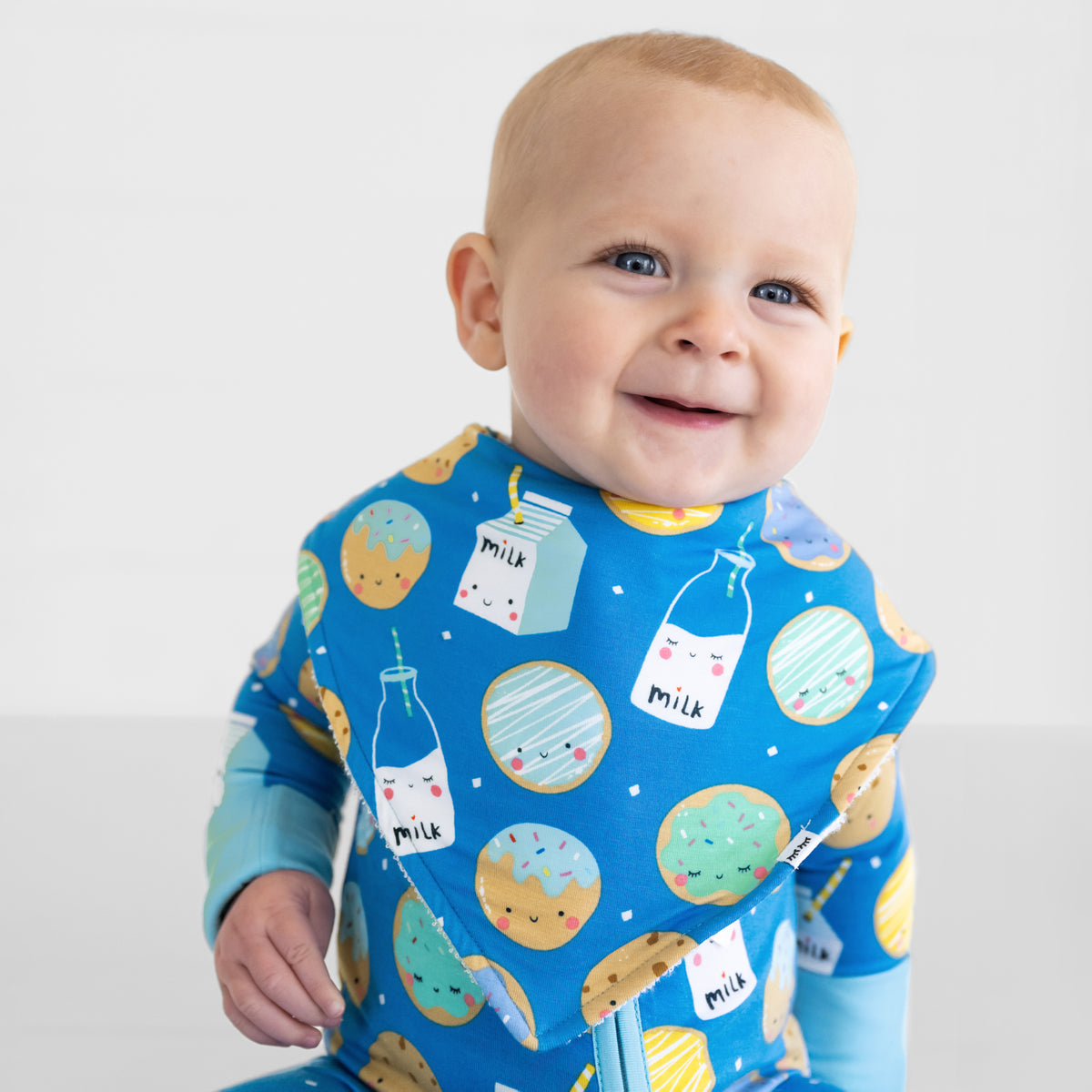 Close up of a smiling baby wearing a Blue Cookies & Milk baby boy bib over matching Blue Cookies & Milk bamboo pajamas