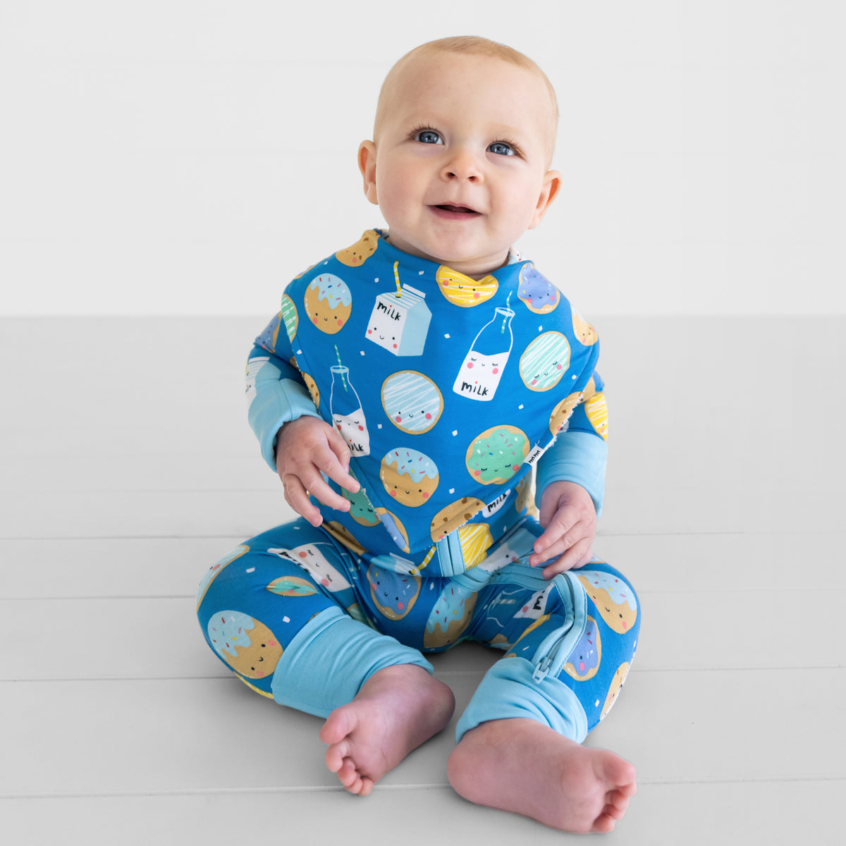 Sitting child wearing a Blue Cookies & Milk baby boy bib over matching Blue Cookies & Milk bamboo pajamas
