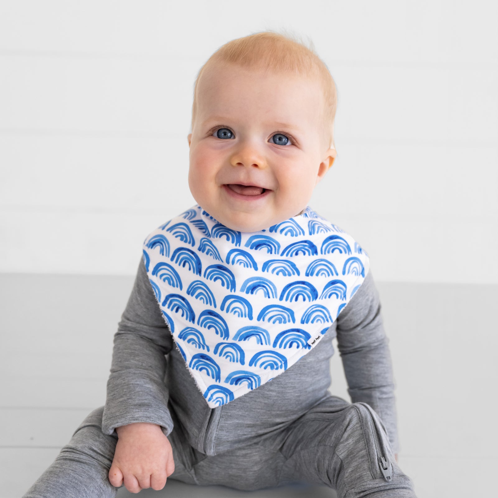 Close up of a child sitting and wearing a Blue Rainbows baby boy bib with a Heather Gray Zippy