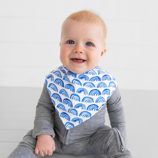 Close up of a child sitting and wearing a Blue Rainbows baby boy bib with a Heather Gray Zippy