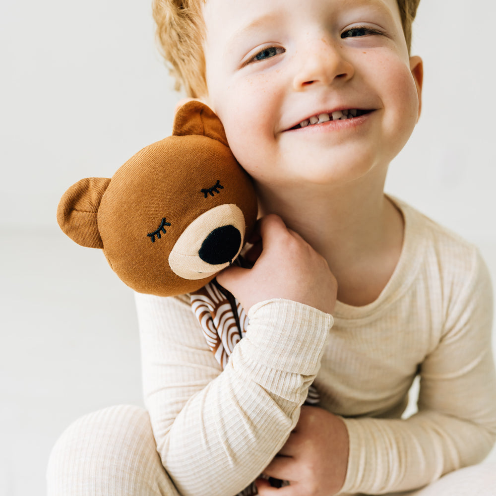 Close up view of a child snuggling a Bowie the Bear Sleepyhead Lovey wearing a Heather Oatmeal Two-Piece Pajama Set