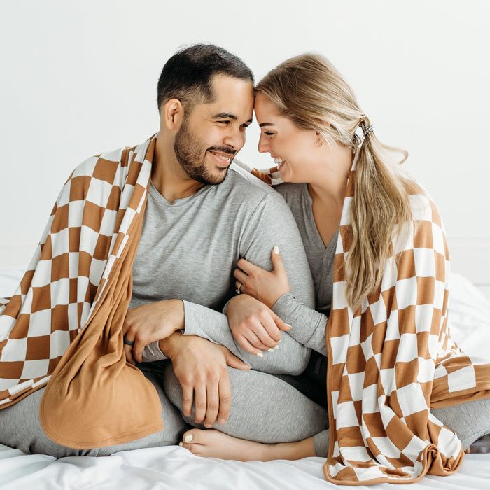 Husband and wife cuddling with a Caramel Checks oversized bamboo blanket wrapped around them