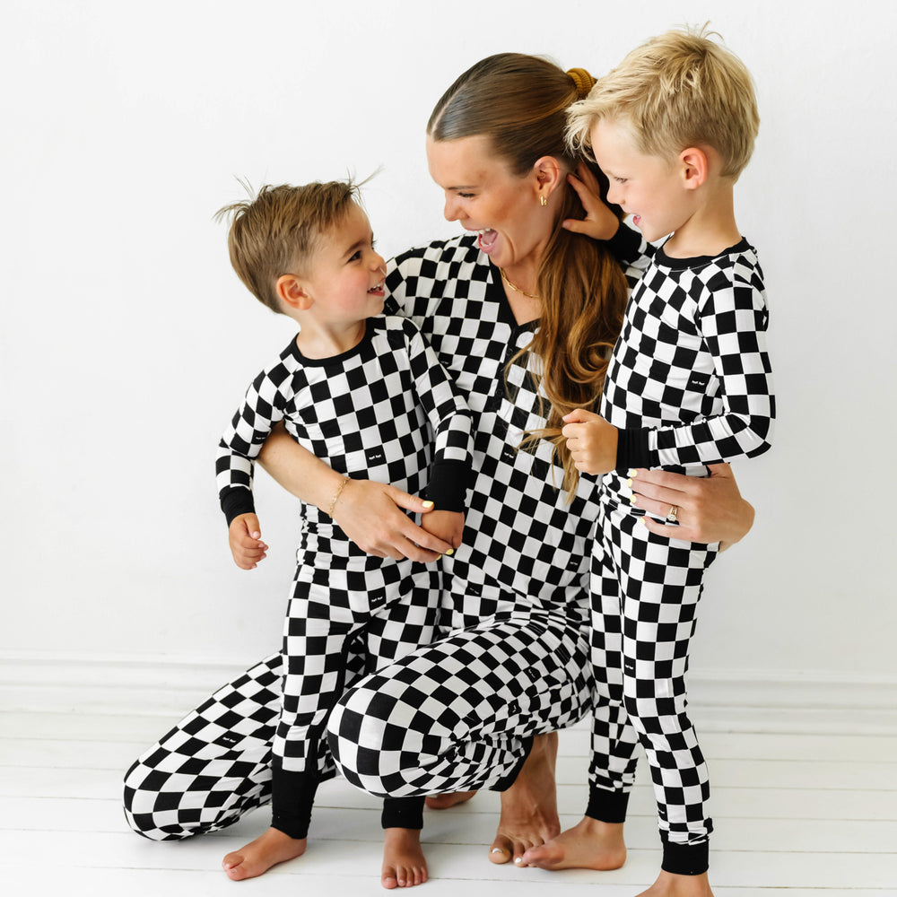 Click to see full screen - Mom kneeling with her two children wearing matching Cool Checks printed pajama sets. Mom is wearing Cool Checks printed women's pajama top and women's pajama pants. Kids are wearing Cool Check printed pajamas in crescent zippy and two piece styles