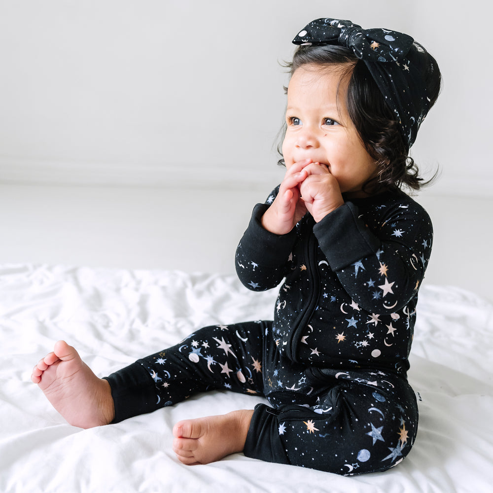 Child sitting on a blanket wearing a Counting Stars printed luxe bow headband and matching zippy