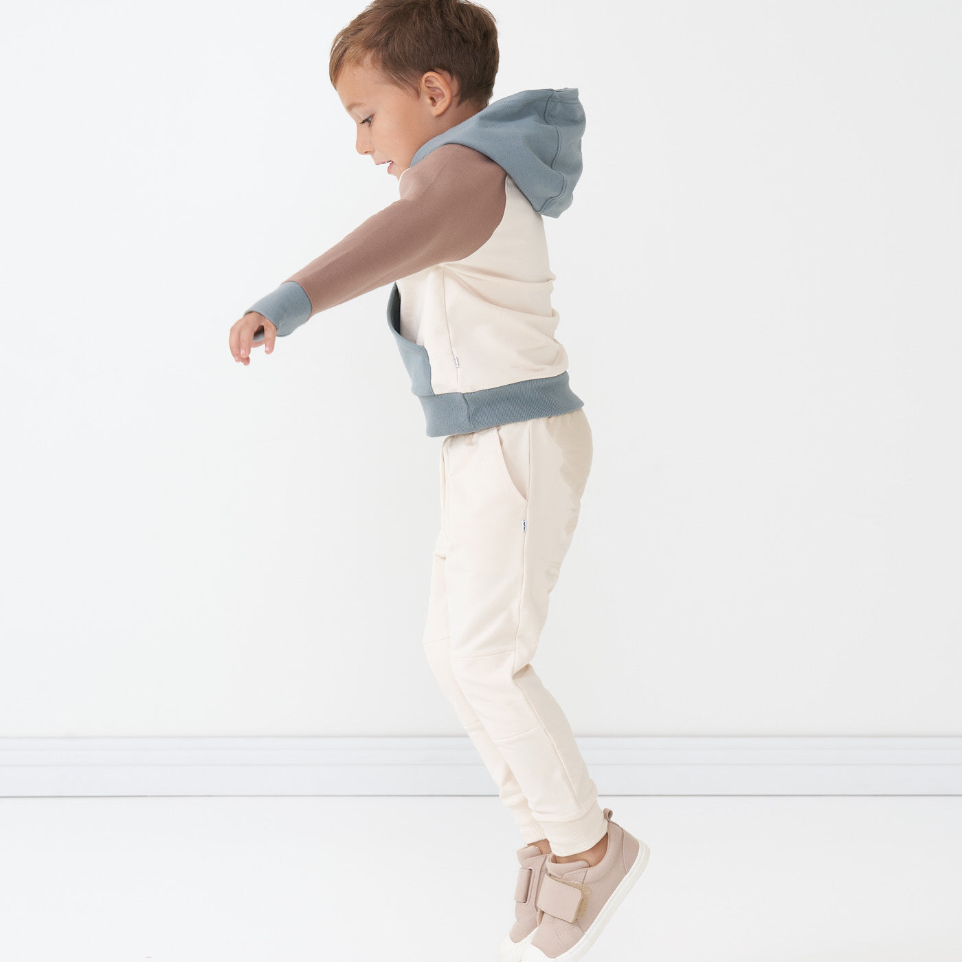 Child jumping wearing Cream joggers and coordinating Colorblock pullover hoodie