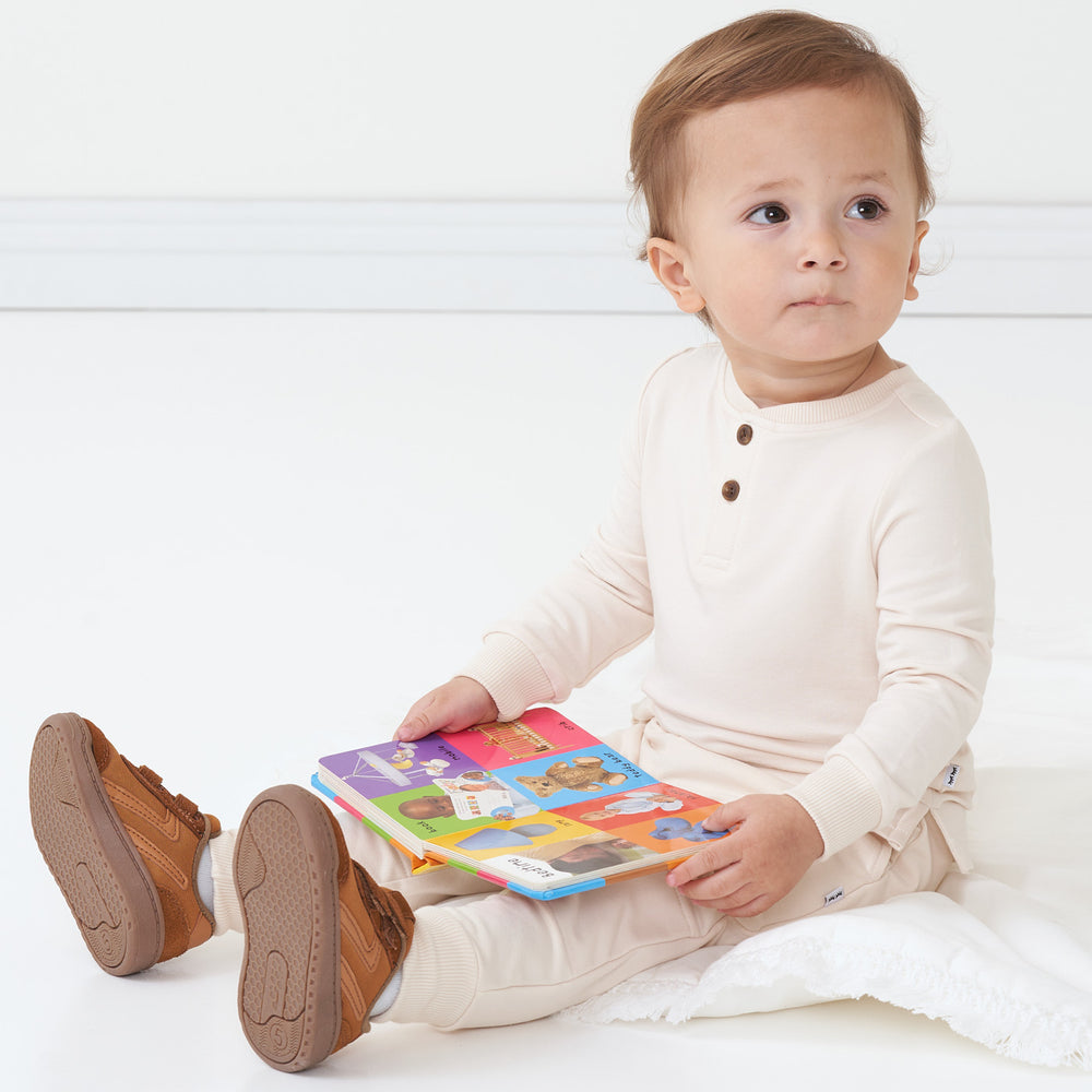 Child reading a book wearing a Cream henley tee and matching joggers
