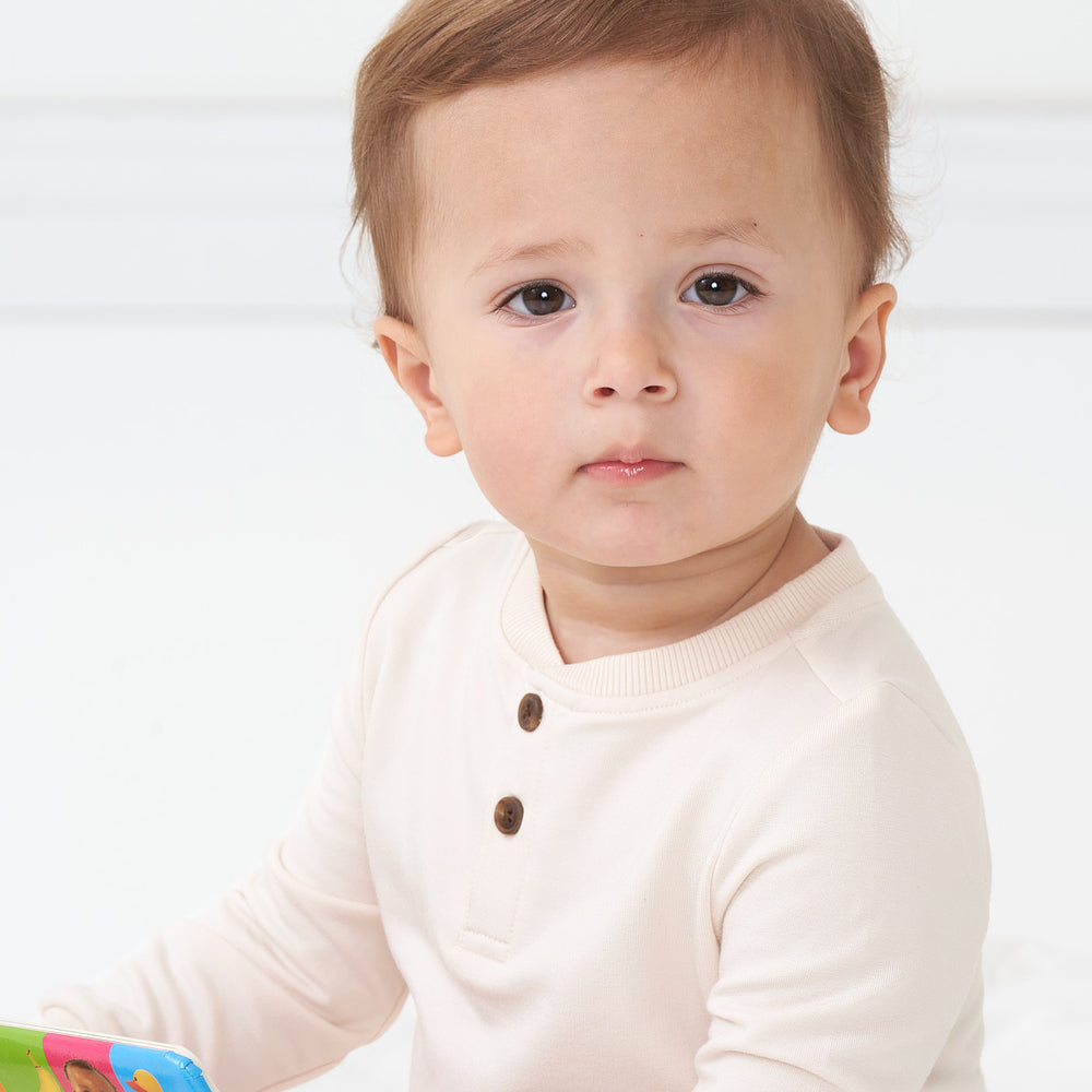 Close up side view image of a child wearing a Cream henley tee