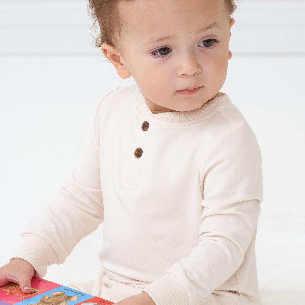 Close up image of a child reading a book wearing a Cream henley tee