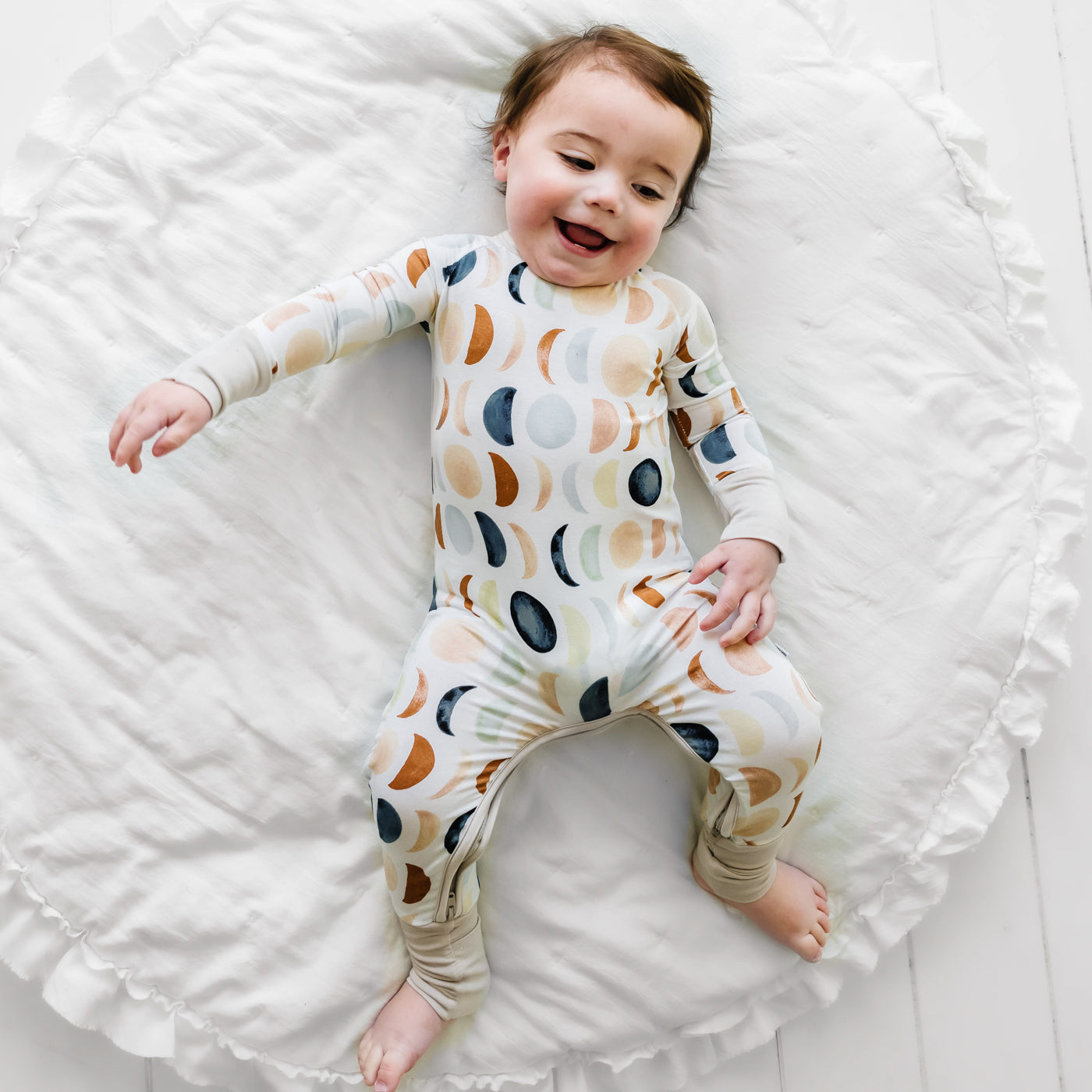 Child laying on a bed wearing a Luna Neutral crescent zippy