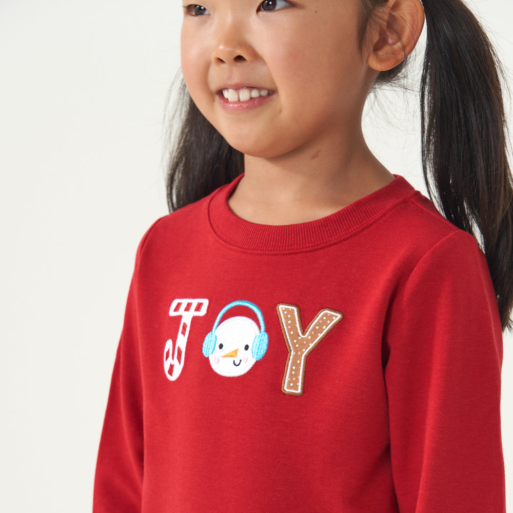 Close up image of a child wearing a Holiday Red Joy crewneck detailing the Joy graphics