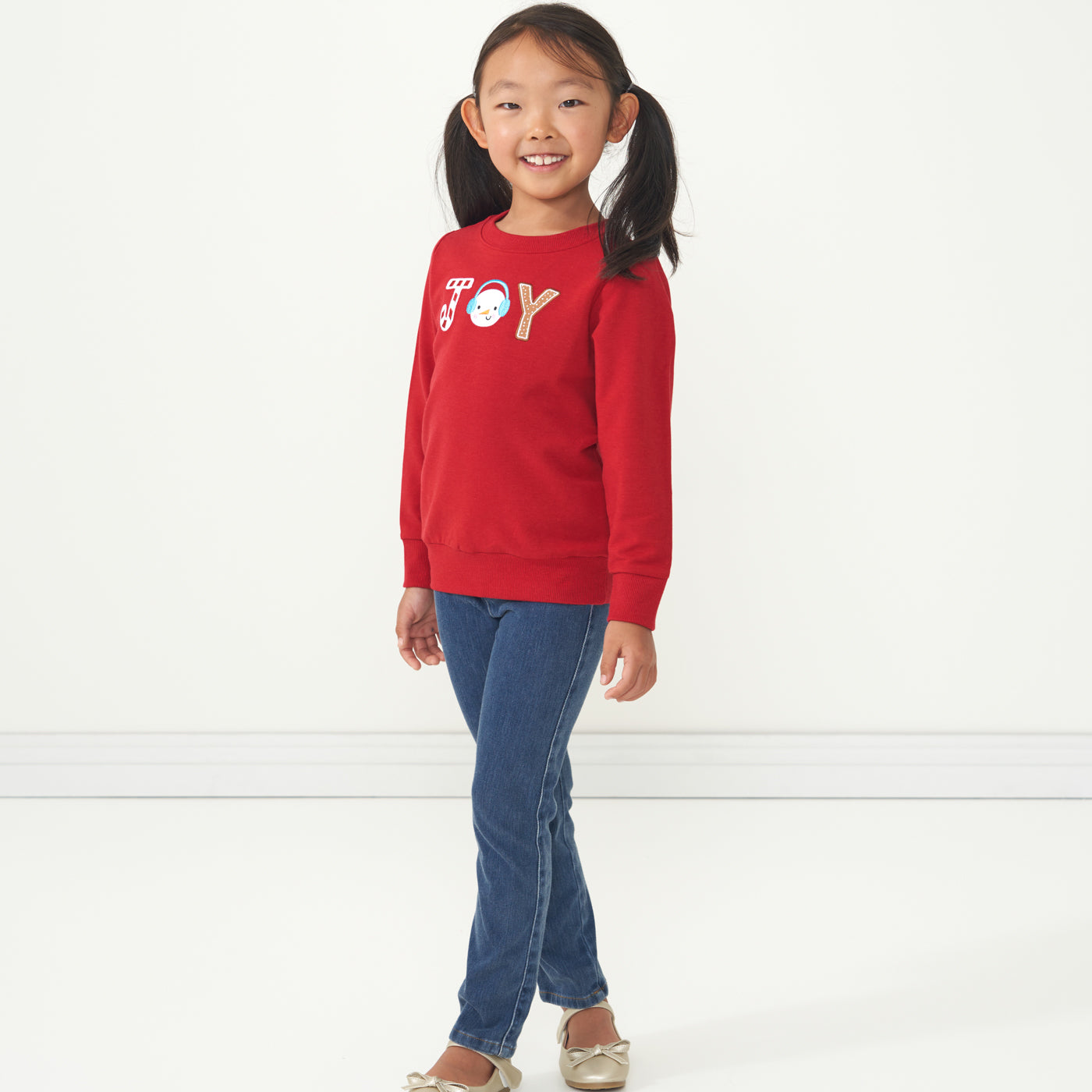 Profile view of a child wearing a Holiday Red Joy crewneck