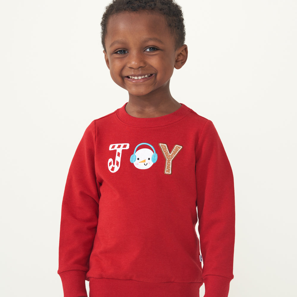 Close up image of a child wearing a Holiday Red Joy crewneck