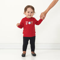 Child wearing a Holiday Red Joy crewneck paired with black leggings