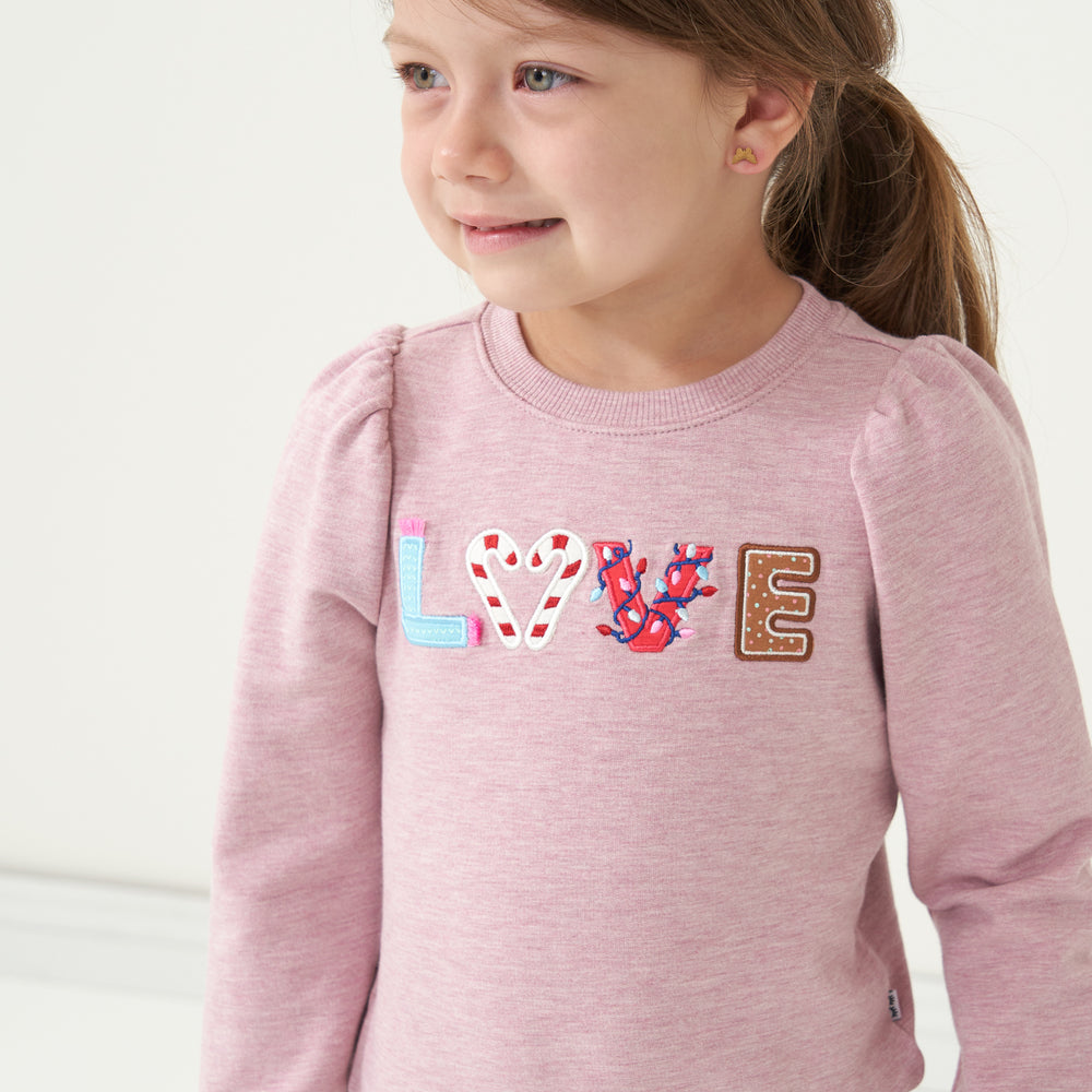 Close up image of a child wearing a Heather Mauve Love puff sleeve crewneck detailing the Love graphic