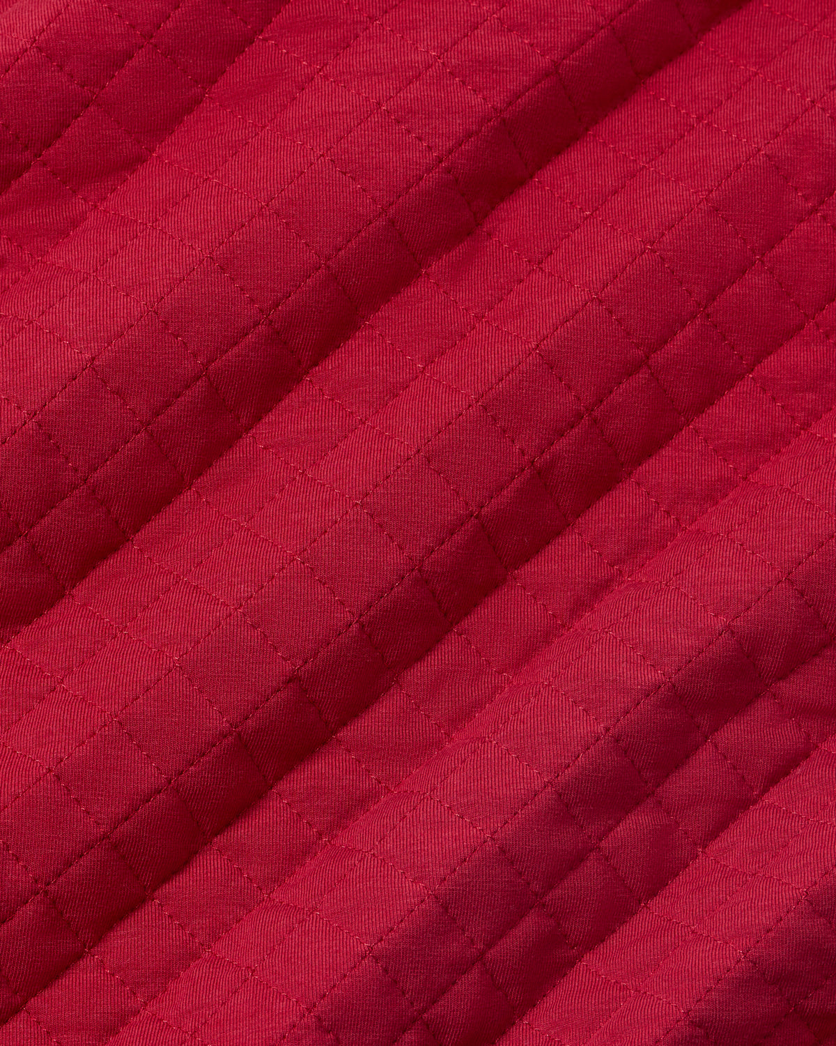 A close-up of a quilted fabric in a rich magenta-red color, showing the diamond stitching pattern and diagonal folds.