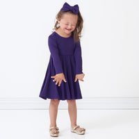 Child laughing wearing a Deep Amethyst ribbed twirl dress and matching luxe bow headband