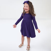 Child spinning around wearing a Deep Amethyst ribbed twirl dress and matching luxe bow headband