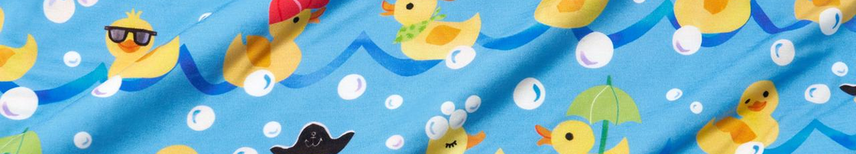 A close-up of a blue fabric with a playful rubber duck pattern, featuring yellow ducks, white soap bubbles, and small accessories like sunglasses, a red hat, and a green umbrella.