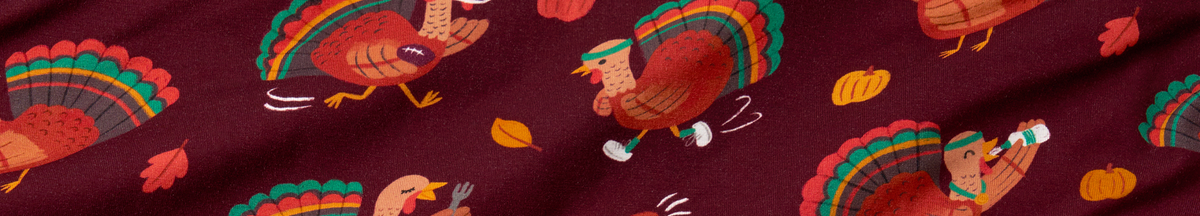 A close-up of a burgundy fabric with a repeating pattern of cartoon turkeys, autumn leaves, and pumpkins in orange, yellow, green, and white.