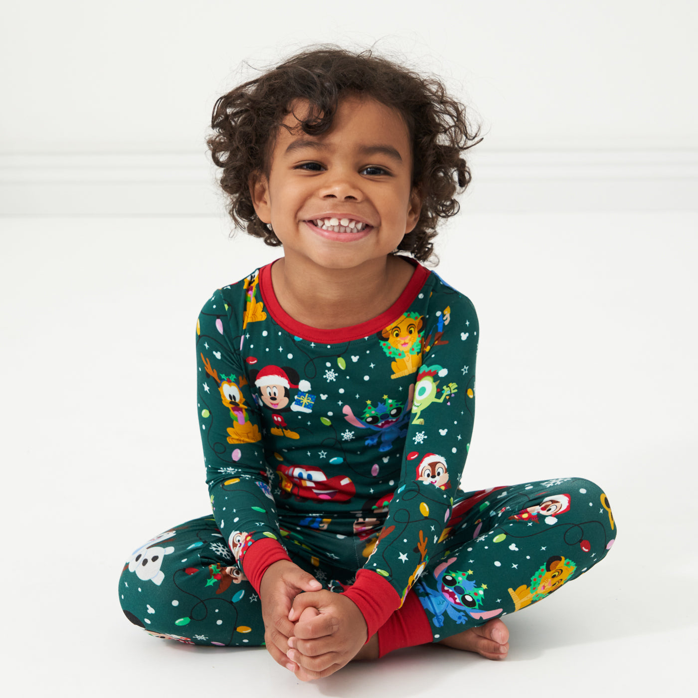 Child sitting on the ground wearing a Disney Christmas Party two piece pajama set
