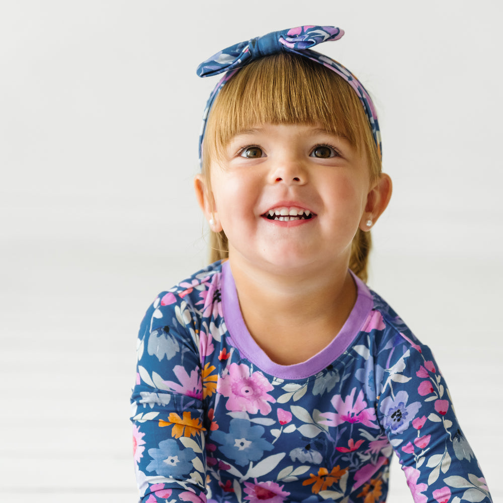 Close up image of a child sitting wearing Dusk Blooms two piece pajama set paired with a matching luxe bow headband