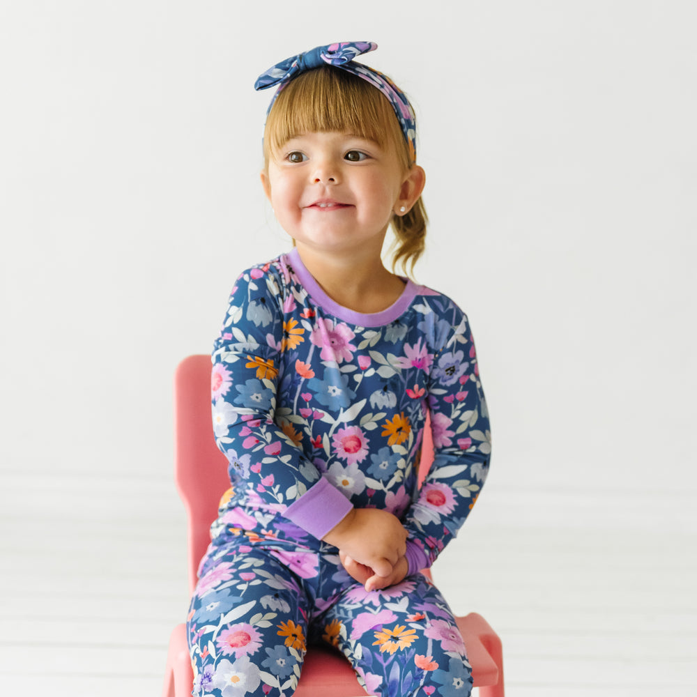 Child sitting wearing Dusk Blooms two piece pajama set paired with a matching luxe bow headband