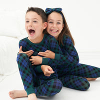 Two children sitting on the ground wearing matching Emerald Plaid two-piece pajama sets