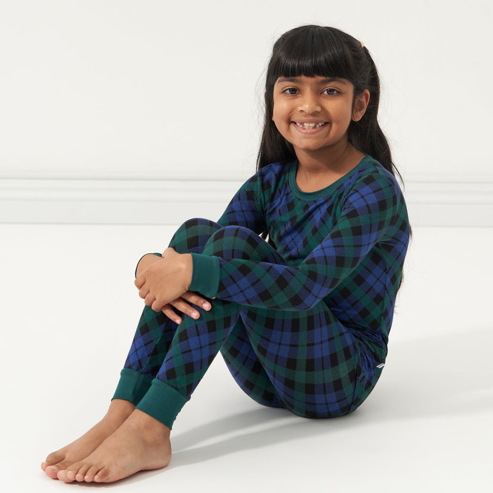 Child sitting on the ground wearing an Emerald Plaid two-piece pajama set