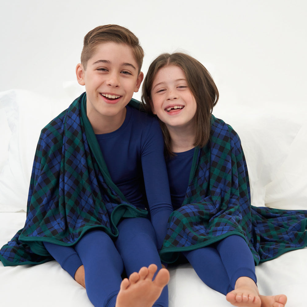 Two children sitting on the ground with an Emerald Plaid large cloud blanket wrapped around them