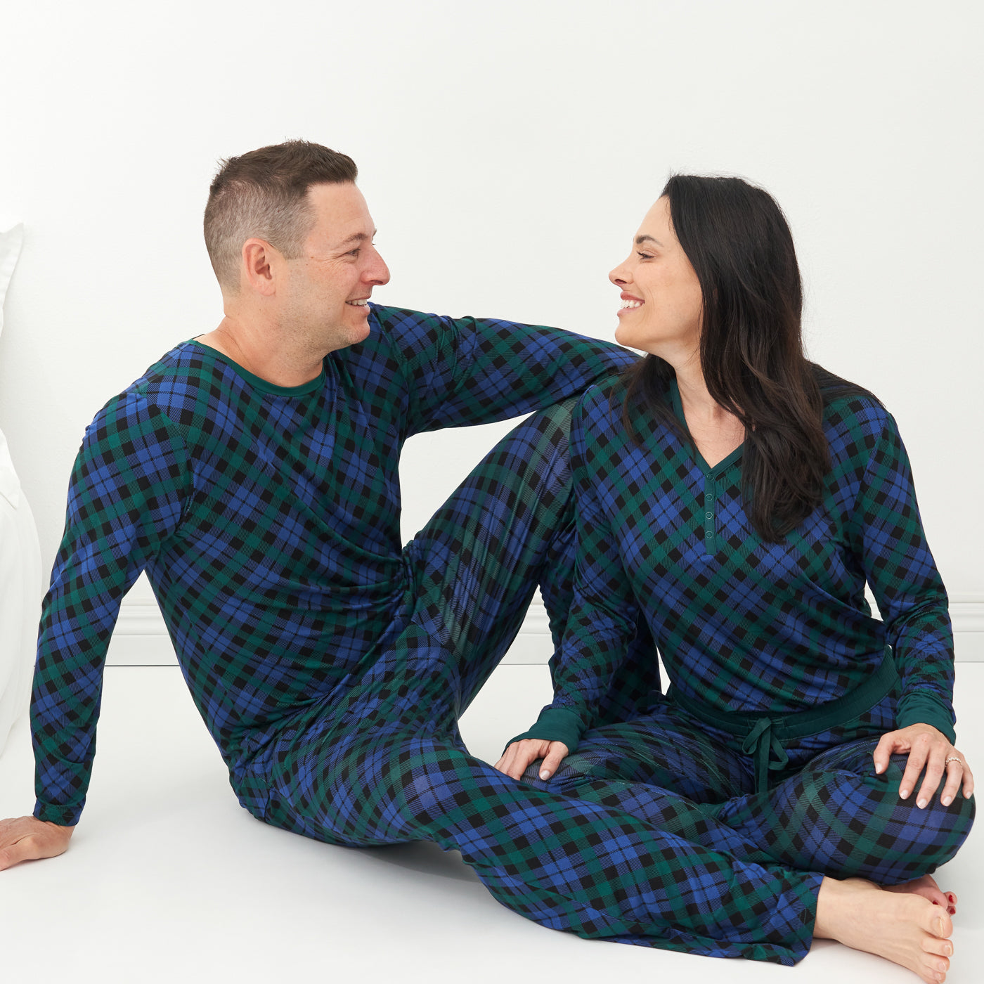 Man and woman sitting on the ground wearing matching Emerald Plaid pajamas