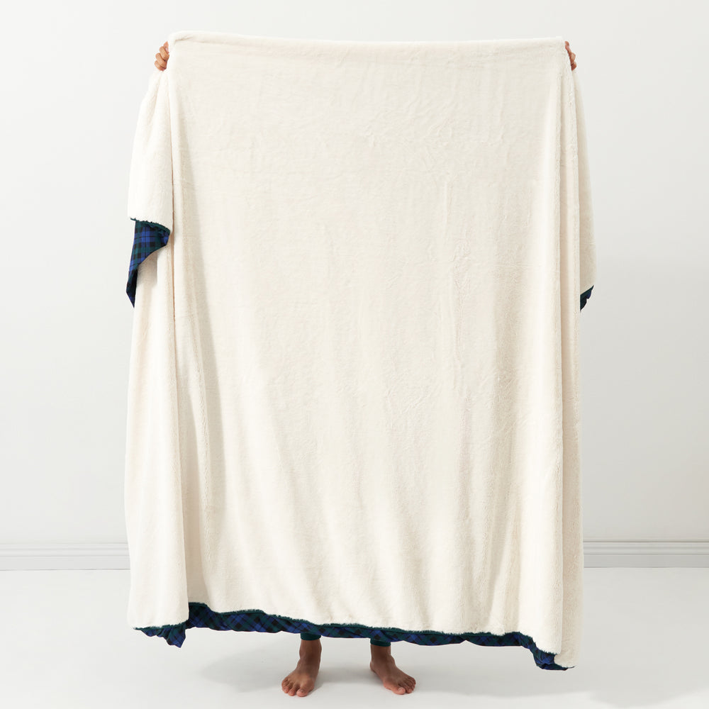 Woman holding up an Emerald Plaid plush oversized cloud blanket in front of her showing the solid white backing