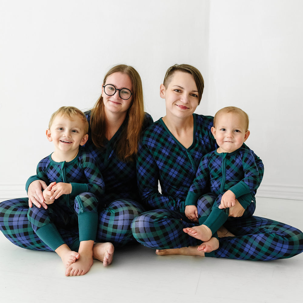 Family of four sitting together wearing Emerald Plaid women's pajama top and bottoms. Children are wearing Emerald Plaid matching zippies