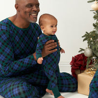 Dad and child sitting in front of a tree wearing matching Emerald Plaid zippy and adult pajamas