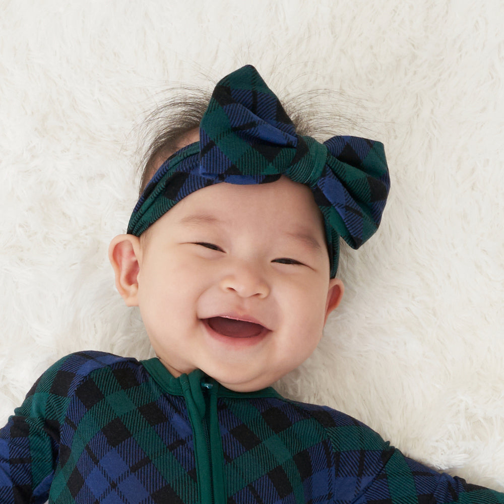 Close up image of a child wearing an Emerald Plaid luxe bow headband paired with a matching zippy