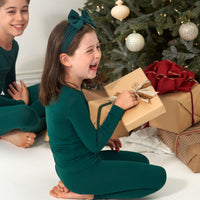 Child holding a present wearing an Emerald luxe bow headband and matching pajamas