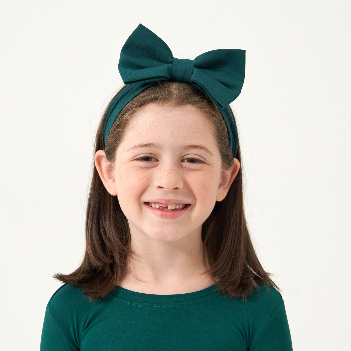 Close up image of a child wearing an Emerald luxe bow headband and matching pajamas