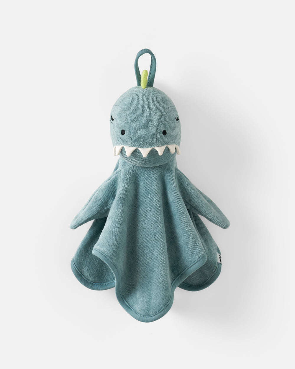 A plush dinosaur-shaped wash towel in dusty blue-green, featuring embroidered eyes and teeth, white teeth, and a small green loop at the top, photographed against a clean white background.