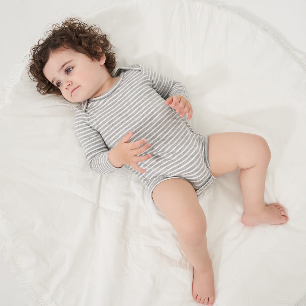 Click to see full screen - Child laying on a bed wearing a Heather Gray and Ivory Stripe bodysuit