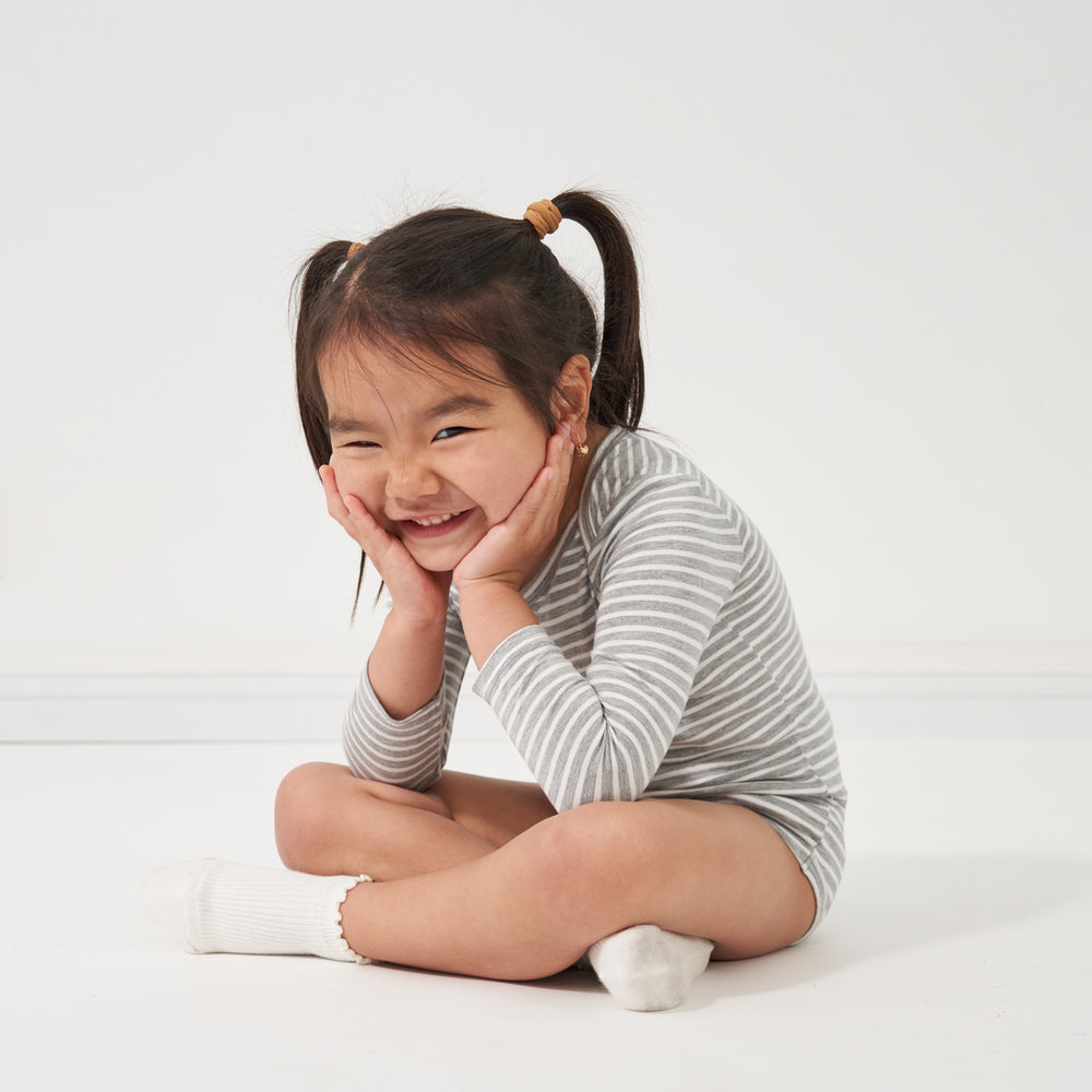 Child sitting and posing wearing a Heather Gray and Ivory Stripe bodysuit