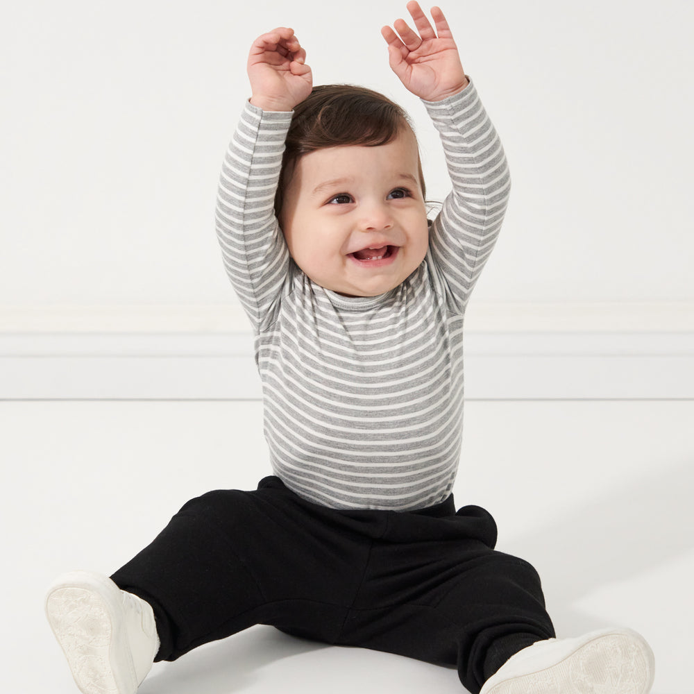 Click to see full screen - Child sitting and wearing a Heather Gray and Ivory Stripe Bodysuit paired with black joggers