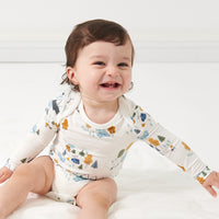 Close up image of a child sitting on the ground wearing a Let's Explore printed bodysuit