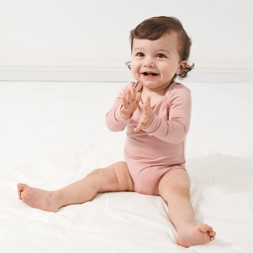 Child sitting on a bed wearing a Mauve Blush bodysuit