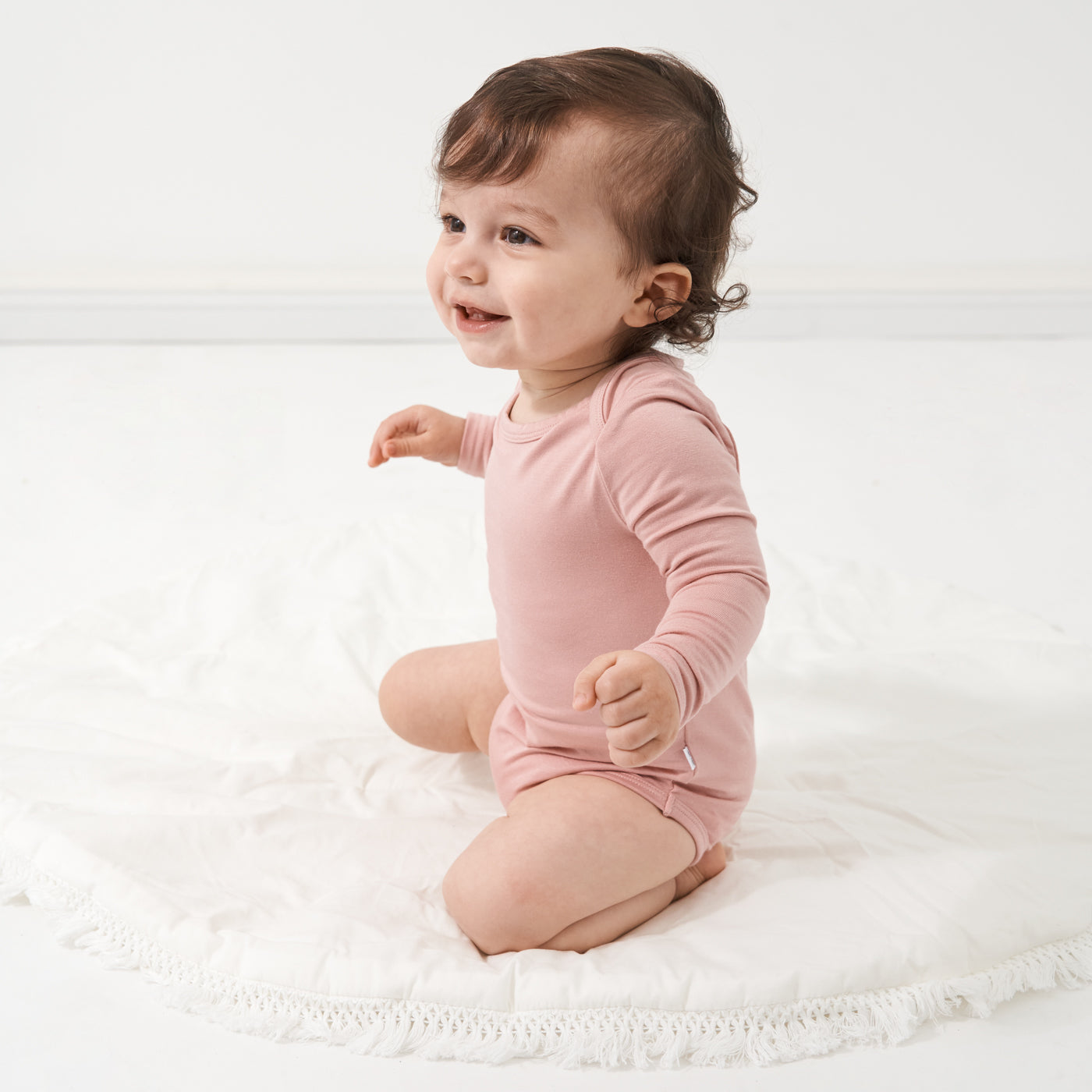 Child playing on a bed wearing a Mauve Blush bodysuit
