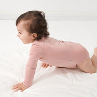 Child crawling on a bed wearing a Mauve Blush bodysuit