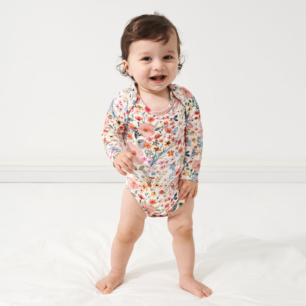 child standing on a bed wearing a Mauve Meadow printed bodysuit