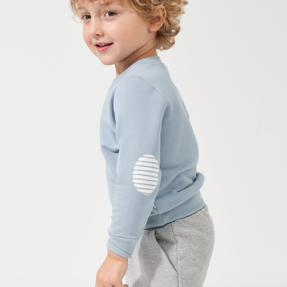 Side view of a child wearing a Fog elbow patch crewneck