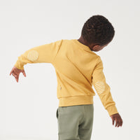 Back view image of a child wearing a Honey elbow patch crewneck