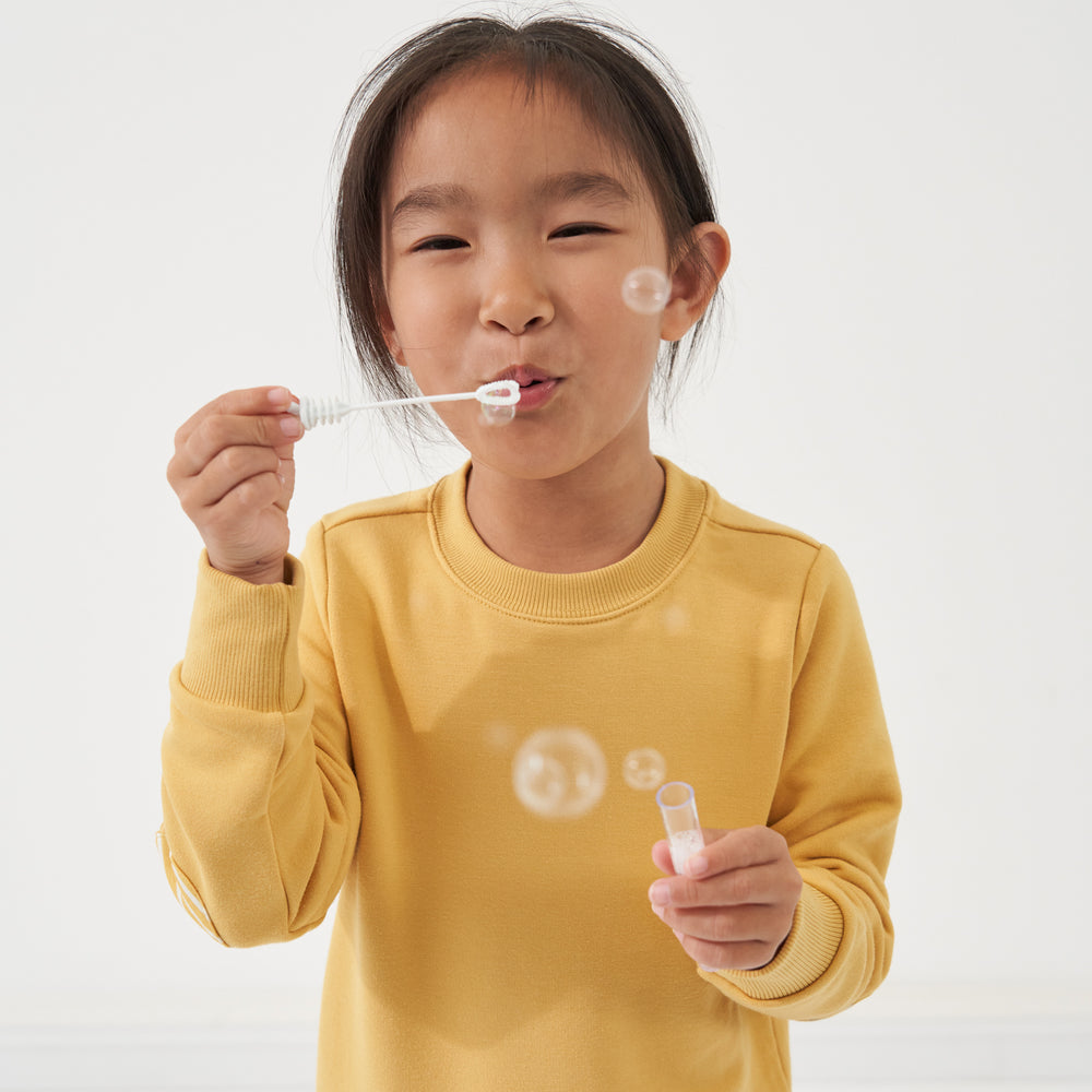 Child blowing bubbles wearing a Honey elbow patch crewneck