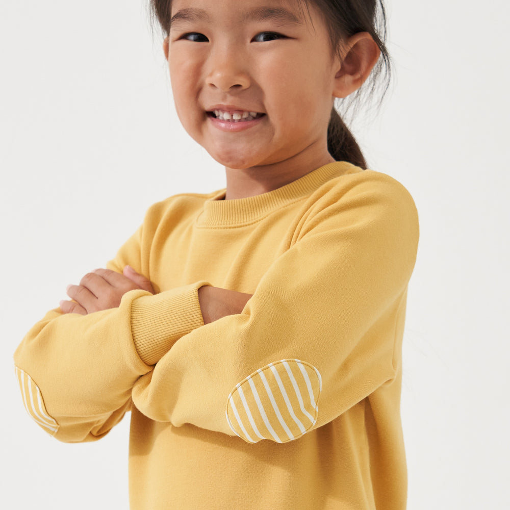 Child with her arms crossed wearing a Honey elbow patch crewneck