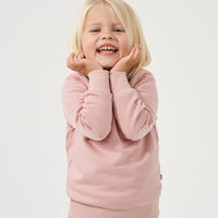 Child posing with her hands under her chin wearing a Mauve Blush crewneck